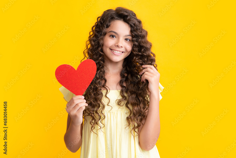 Happy teenager portrait. Cheerful lovely romantic teen girl hold red heart symbol of love for valentines day isolated on yellow background. Smiling girl. Happy teenager portrait. Cheerful lovely romantic teen girl hold red heart symbol of love for valentines day isolated on yellow background. Smiling girl.