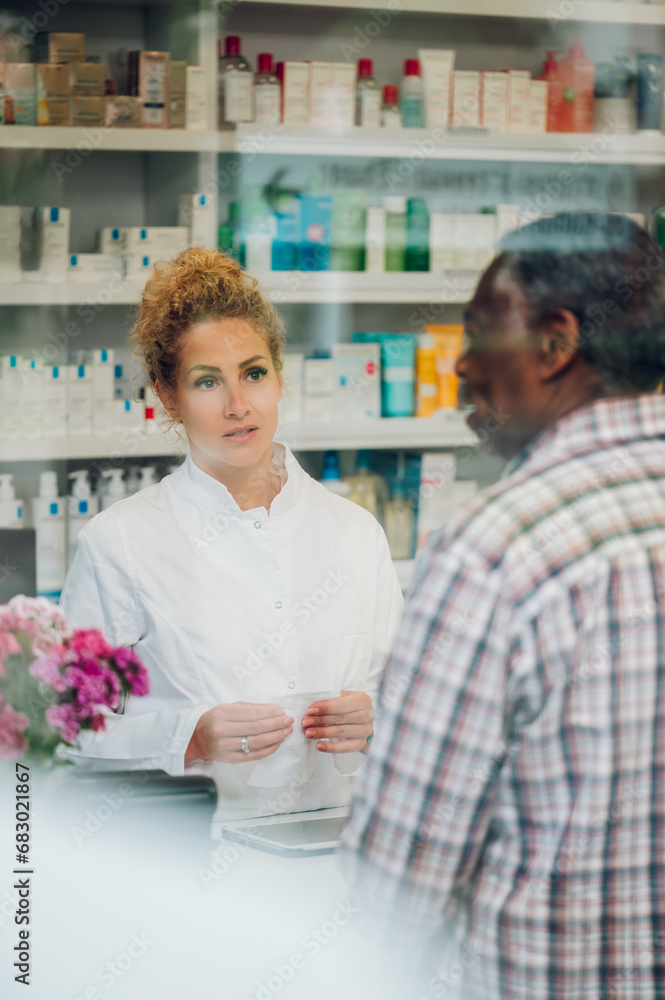 View through the window of a pharmacist selling medicament to a senior african american man.