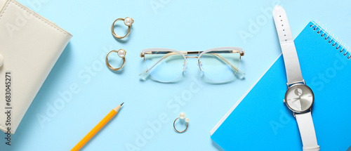 Eyeglasses with jewelry rings, wristwatch and stationery on light blue background