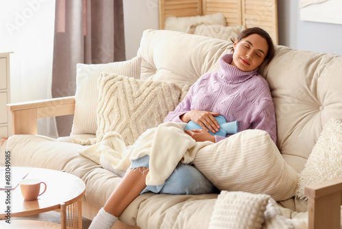 Young woman with hot water bottle sitting on sofa at home photo