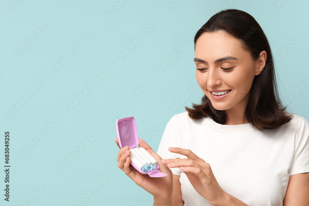 Beautiful young woman with tampons storage box on blue background Beautiful young woman with tampons storage box on blue background