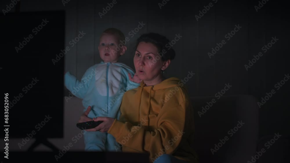 woman with a little daughter watches TV in the evening and switches TV channels. High quality 4k footage woman with a little daughter watches TV in the evening and switches TV channels. High quality 4k footage
