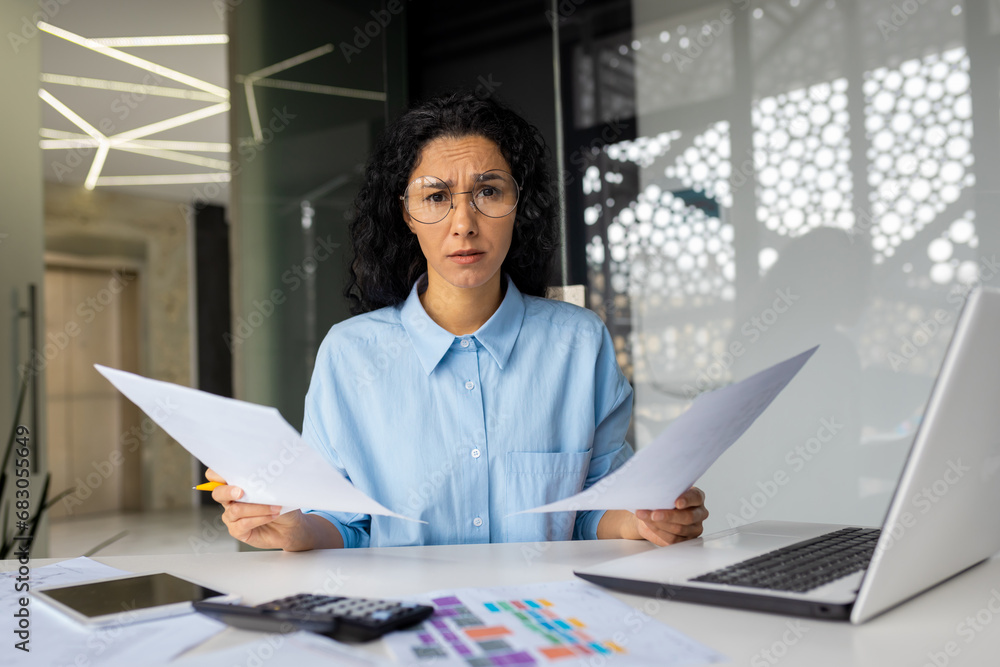 Dissatisfied upset woman looking at camera, business woman holding reports financial contracts papers, female worker inside office working on paperwork, checking and analyzing.