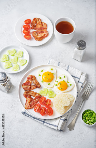 Fresh breakfast with fried eggs, fried bacon slices, bread slices and vegetables in the form of heart for Valentine's day holiday
