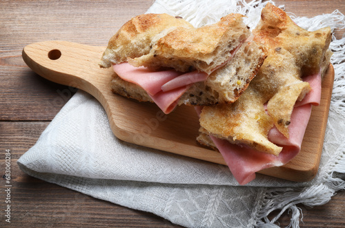 Wholemeal focaccia with mortadella on wooden background with cutting board and napkin, close-up.