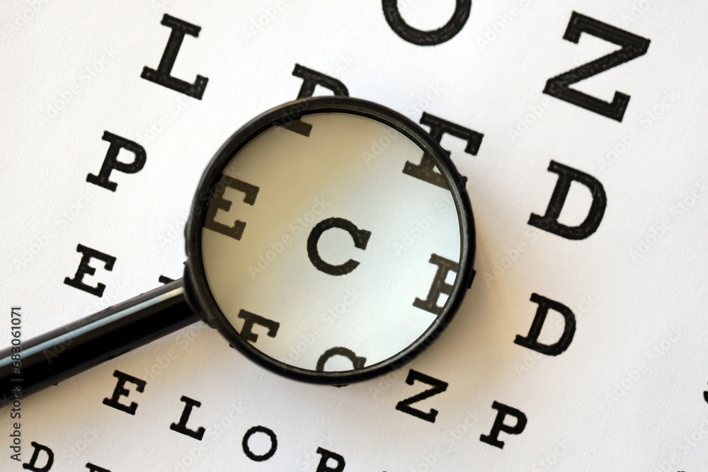 Magnifier glass focuses eye chart letters clearly and lies on eye test chart paper close up Magnifier glass focuses eye chart letters clearly and lies on eye test chart paper close up