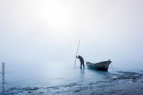 Fototapeta Naklejka Na Ścianę i Meble -  The story of a fisherman who wants to make a way for herself on a frozen lake on winter days and tries to get her fishing boat out of the ice. 