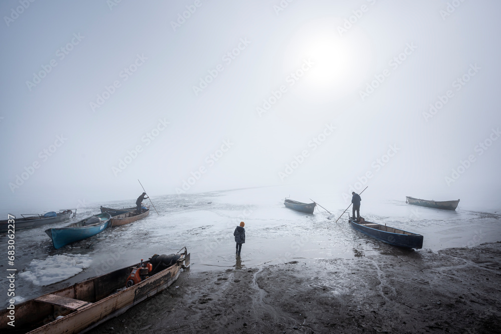 The story of a fisherman who wants to make a way for herself on a frozen lake on winter days and tries to get her fishing boat out of the ice.  - obrazy, fototapety, plakaty 