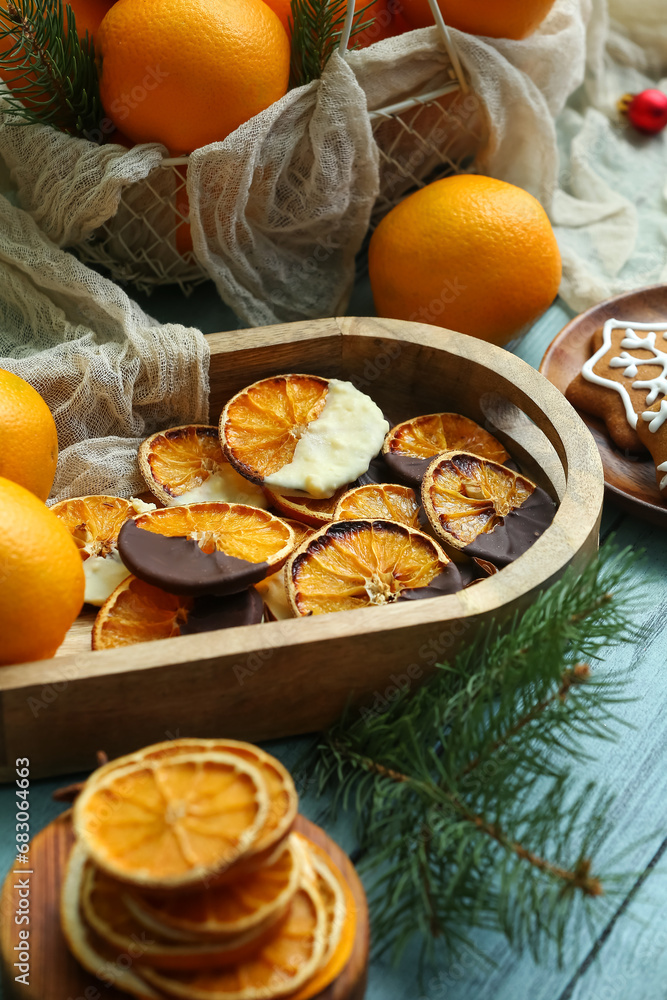 Tray with chocolate dipped dried orange slices, fresh fruits and fir branch on blue wooden background