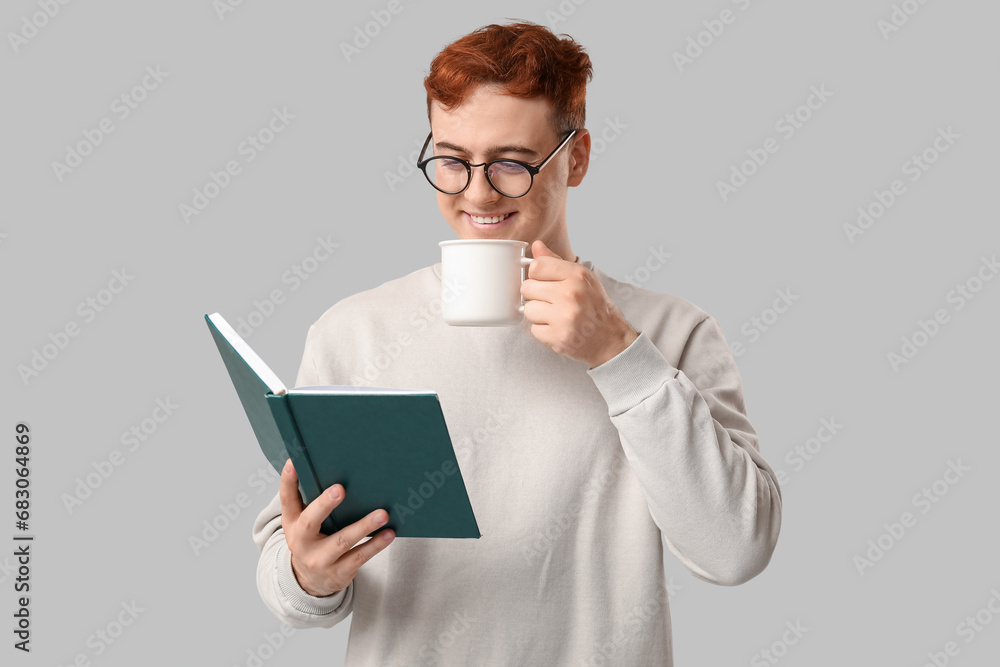 Young man drinking hot beverage and reading book on grey background Young man drinking hot beverage and reading book on grey background
