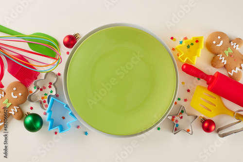 Baking holiday confections concept. Top view shot of green plate, candies, xmas balls, baking equipment, baking molds, colorful stars on light beige background
