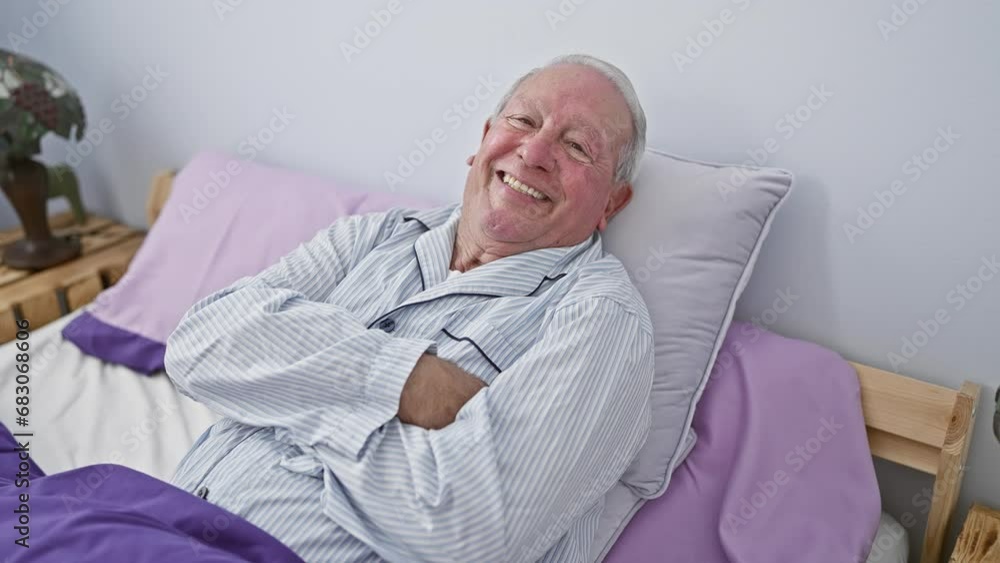 Smiling senior man brimming with positivity, sitting on a bed in his cosy home, crossing arms confidently in pyjamas, engaging a cheerful look at the camera in his bedroom. Smiling senior man brimming with positivity, sitting on a bed in his cosy home, crossing arms confidently in pyjamas, engaging a cheerful look at the camera in his bedroom.