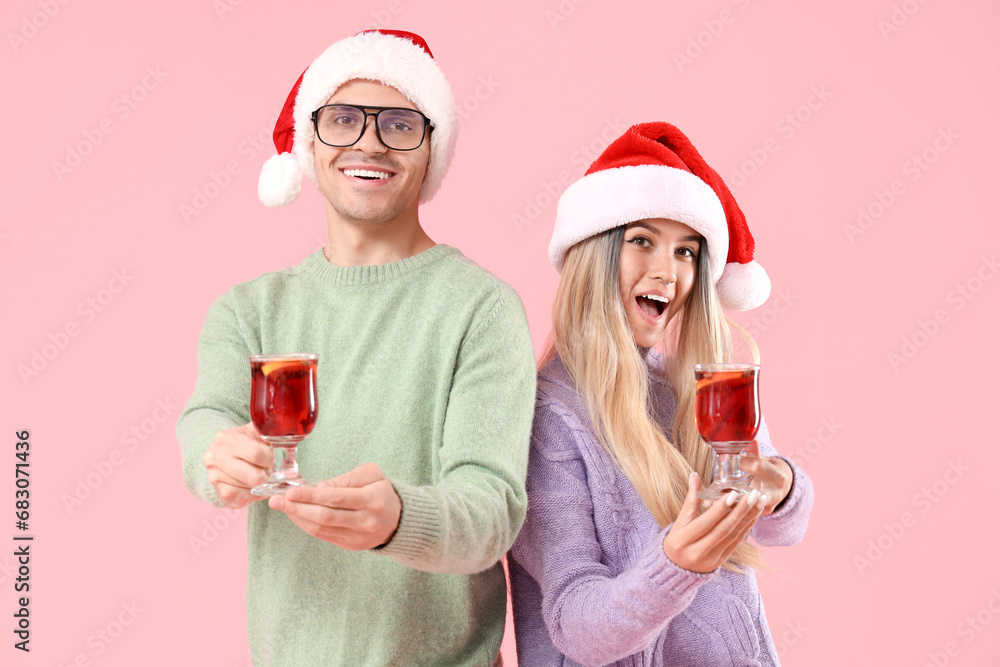 Happy young couple in Santa hats with mulled wine on pink background Happy young couple in Santa hats with mulled wine on pink background