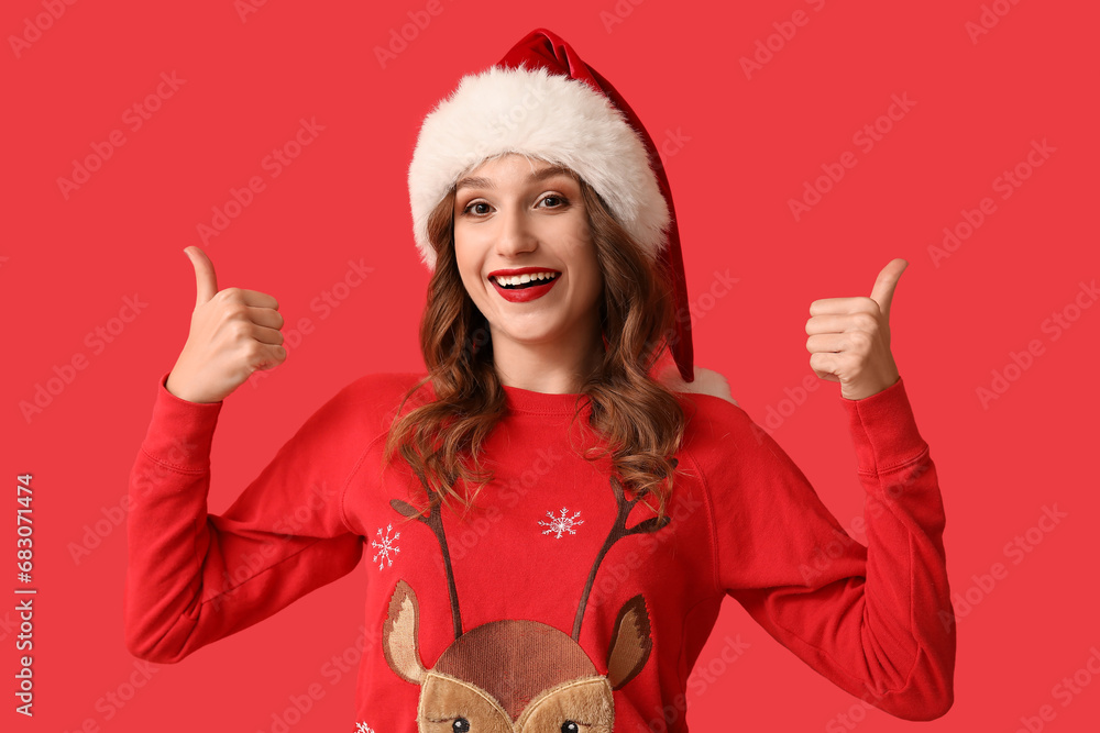 Young woman in Santa hat showing thumb-up gesture on red background Young woman in Santa hat showing thumb-up gesture on red background