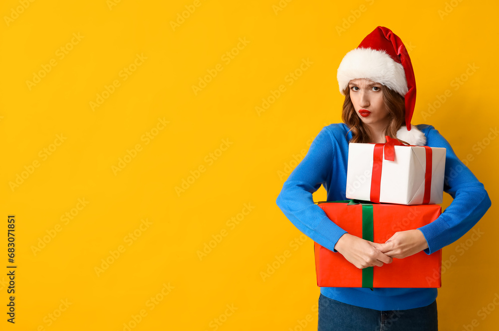 Young woman in Santa hat with Christmas gift boxes on yellow background Young woman in Santa hat with Christmas gift boxes on yellow background