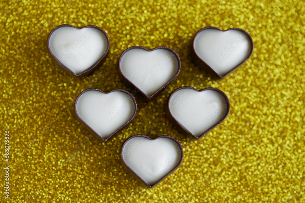 Obraz premium Unusual heart-shaped chocolates made of dark and white Belgian chocolate. Festive golden background for Valentine's Day. Photo. Bokeh. Selective focusing