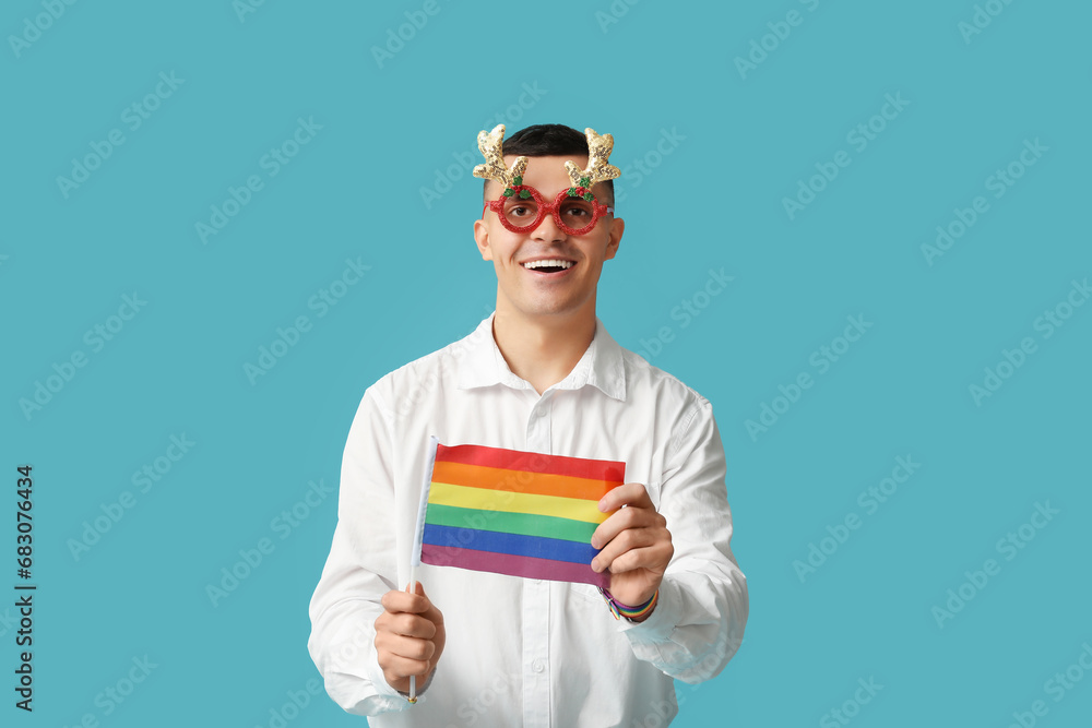 Young man in Christmas eyeglasses with LGBT flag on blue background Young man in Christmas eyeglasses with LGBT flag on blue background