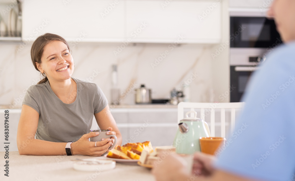While in kitchen, girl drinks tea and chats cheerfully with man