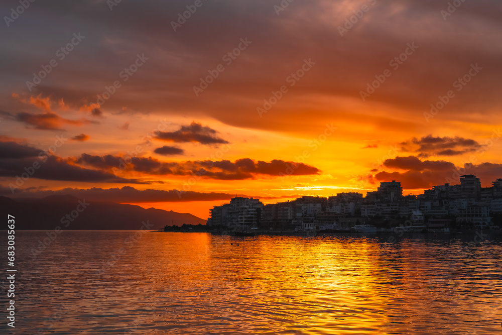 Red sunset at the beach with town in silhouette and dramatic sky with clouds. Amazing sunlight seascape with houses