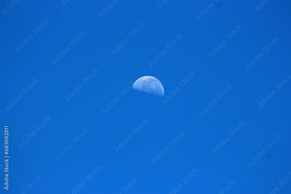 A half moon visible in the morning blue sky A half moon visible in the morning blue sky