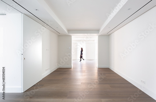 Minimalist hallway with hardwood floors and an unrecognizable woman walking through, surrounded by white walls and natural light photo