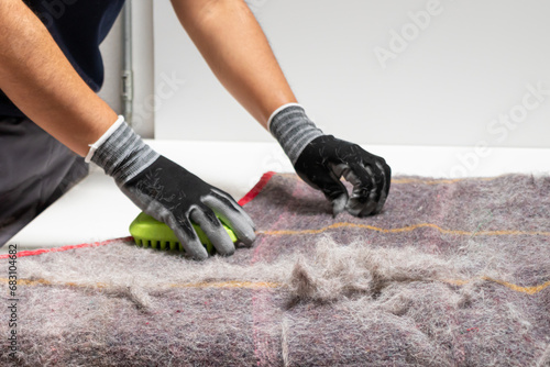 From above cropped unrecognizable person's hands in gloves using a fur removal tool to clean a pet hair-covered blanket photo