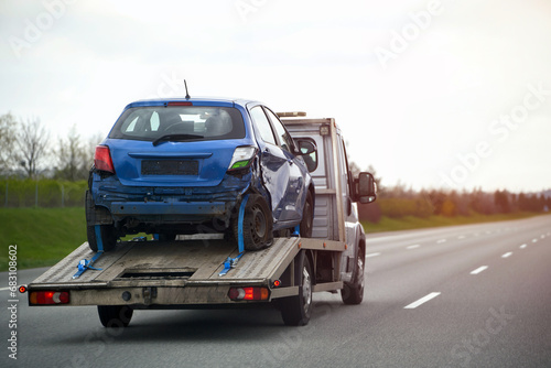 A Side View Of The Tow Truck While Overtaking The Car On The Highway With A Damaged Hatch Back Vehicle After The Traffic Accident. Worldwide 24 Hours A Day Emergency Roadside Assistance