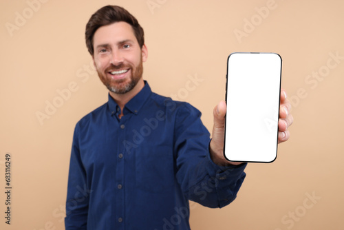 Handsome man showing smartphone in hand on light brown background, selective focus. Mockup for design