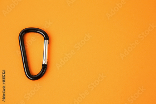 One black carabiner on orange background, top view. Space for text