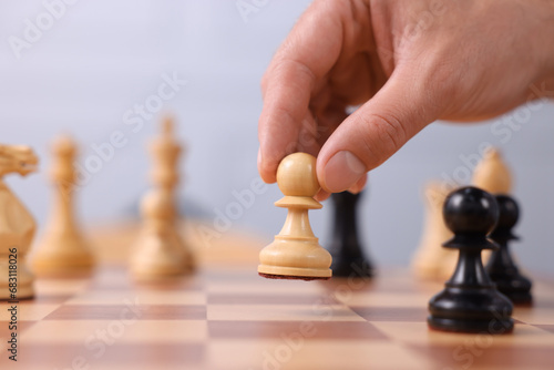 Man with game piece playing chess at checkerboard  closeup. Space for text