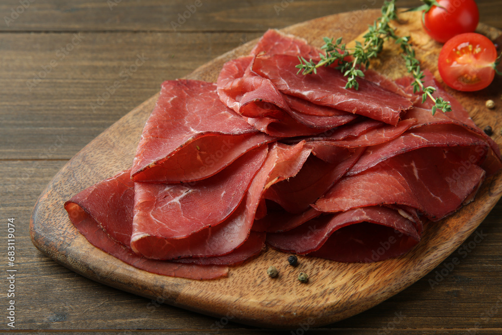 Tasty bresaola, peppercorns, tomatoes and thyme on wooden table, closeup Tasty bresaola, peppercorns, tomatoes and thyme on wooden table, closeup