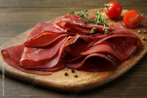 Tasty bresaola, peppercorns, tomatoes and thyme on wooden table, closeup