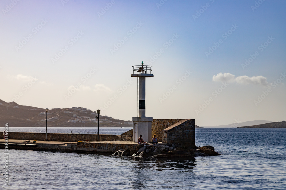 People sitting near the lighthouse in Mykonos, Greece