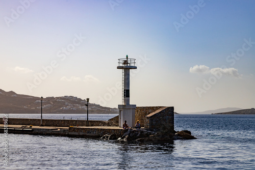People sitting near the lighthouse in Mykonos, Greece