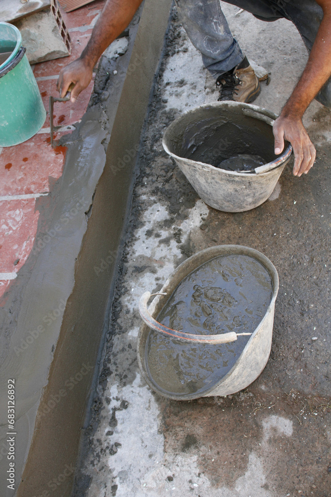 Manos de hombre con dos cubos llenos de mezcla de cemento, empañetando el borde de la acera con una paleta