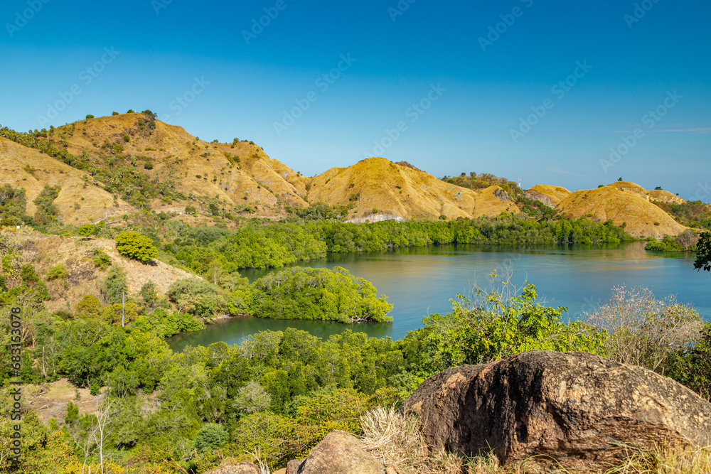 Fototapeta premium Where mountains meet the sea, Labuan Bajo unveils its coastal wonders. Majestic hills embrace the shoreline, creating a breathtaking panorama that captures the essence of nature's harmony.