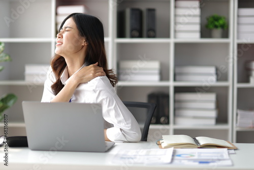 Asian woman working hard in the office having aches and pains in her torso and shoulders. photo