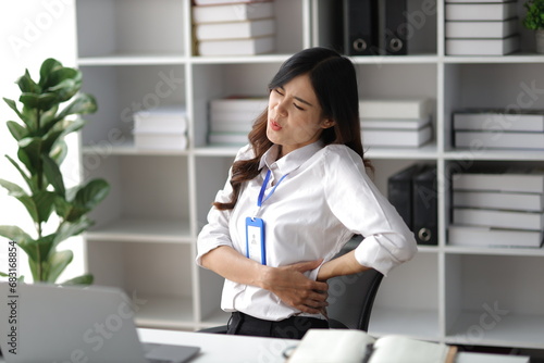 Asian woman working hard in the office having aches and pains in her torso and waist photo