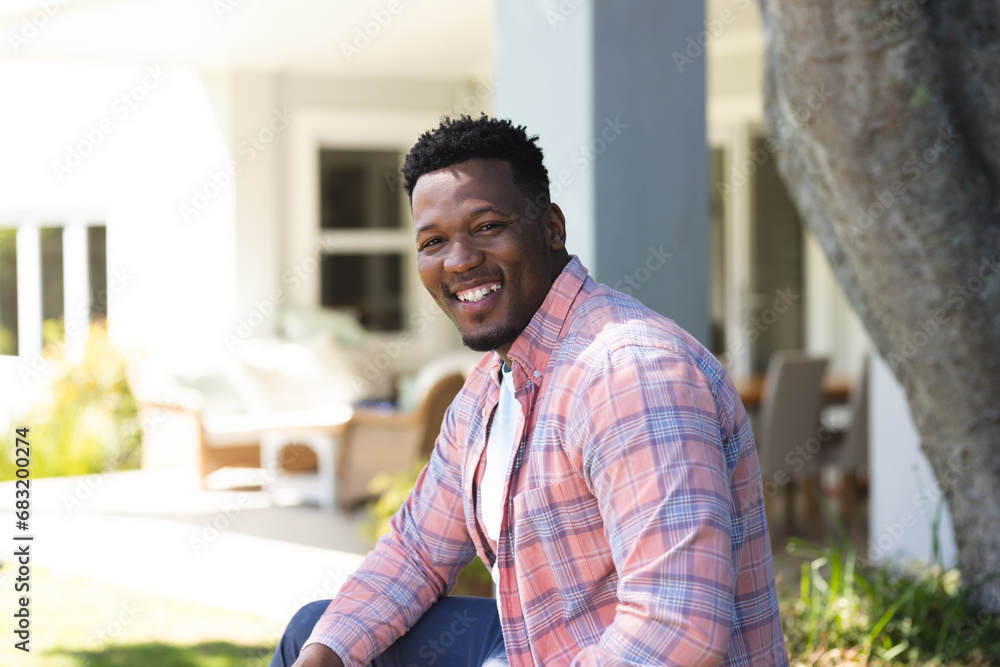 Fototapeta premium Happy african american man sitting with hands on leg in sunny garden, copy space