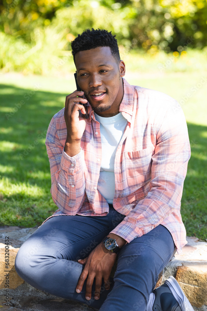 African american man sitting on stairs and talking on smartphone in sunny garden, copy space African american man sitting on stairs and talking on smartphone in sunny garden, copy space