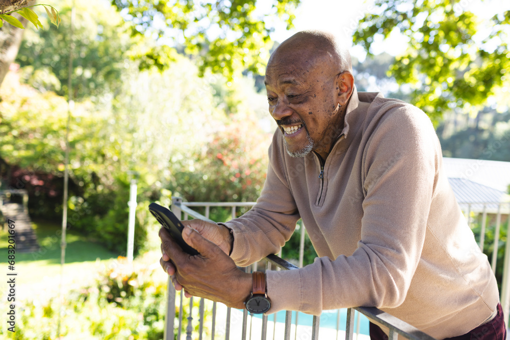 Fototapeta premium Happy african american senior man using smartphone on sunny terrace