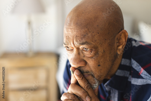 Thoughtful african american senior man sitting on bed in sunny bedroom