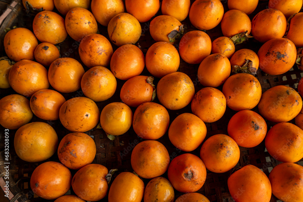 Ripe orange persimmons. on the table in the market. A bunch of organic persimmon fruits at a local farmers market in Dalat city, Vietnam. Persimmon background. Flat lay.