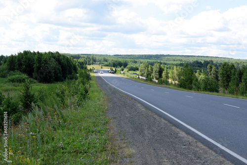 Cars on the highway. Dense forest along the road. Beautiful summer landscape, white clouds on a blue sky.