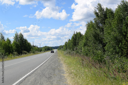 Cars on the highway. Road along the forest. Beautiful summer landscape, white clouds on a blue sky.