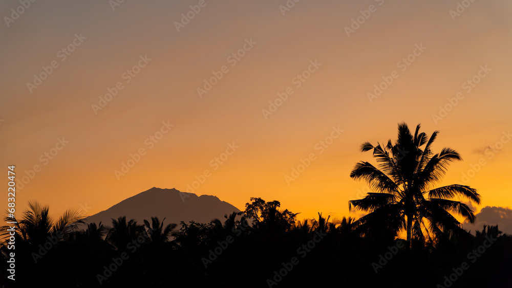 Sunset on a tropical island. The sun illuminates the sky against the background of the silhouette of the volcano and the jungle.