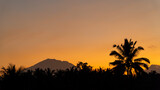 Sunset on a tropical island. The sun illuminates the sky against the background of the silhouette of the volcano and the jungle.