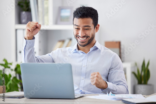 Asian man, success fist and laptop by desk with happy, stock market deal and investment portfolio growth in office. Profit, winner hands and smile by computer with technology and online with cheering photo