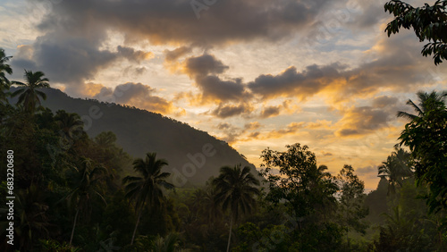 Sunset on a tropical island. The sun illuminates the sky against the background of the silhouette of the mountain and the jungle.