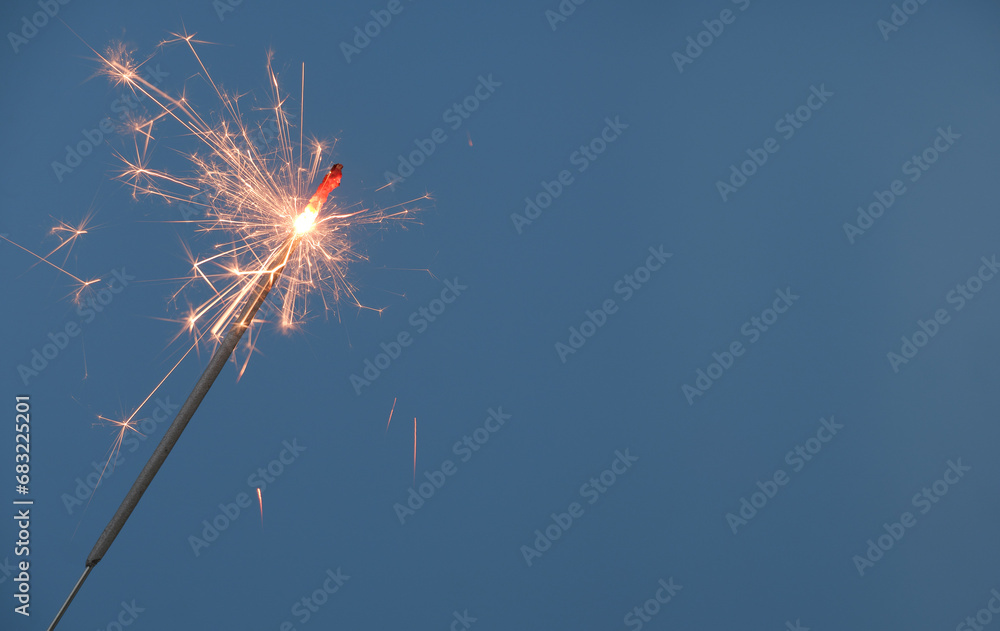 Christmas sparkler burning on blue background, copy space for text.